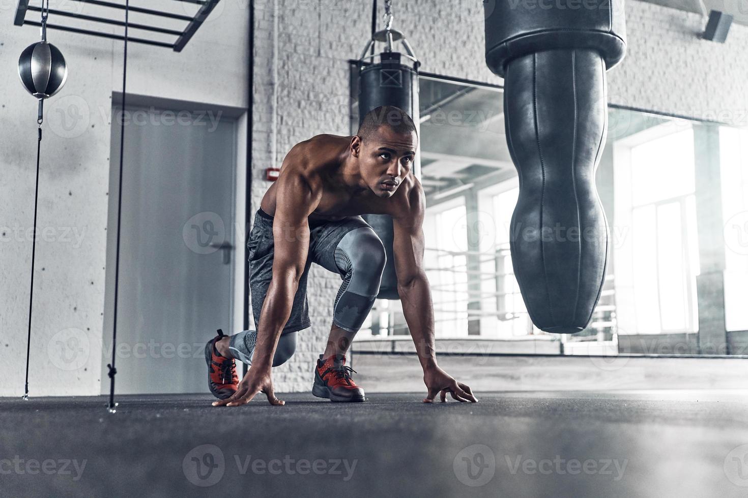 Ready to start. Shirtless young African man position for a race while exercising in the gym photo