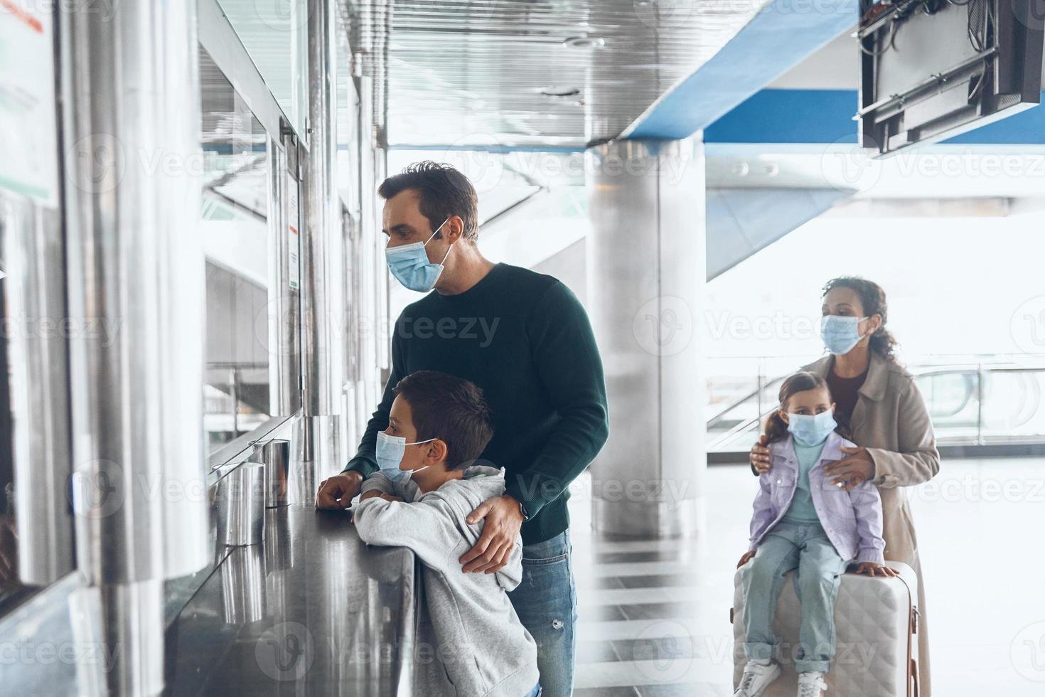 Family with two little kids in protective face masks buying tickets at ticket counter photo