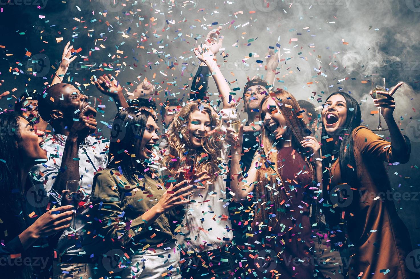 Fun in motion. Group of beautiful young people throwing colorful confetti while dancing and looking happy photo