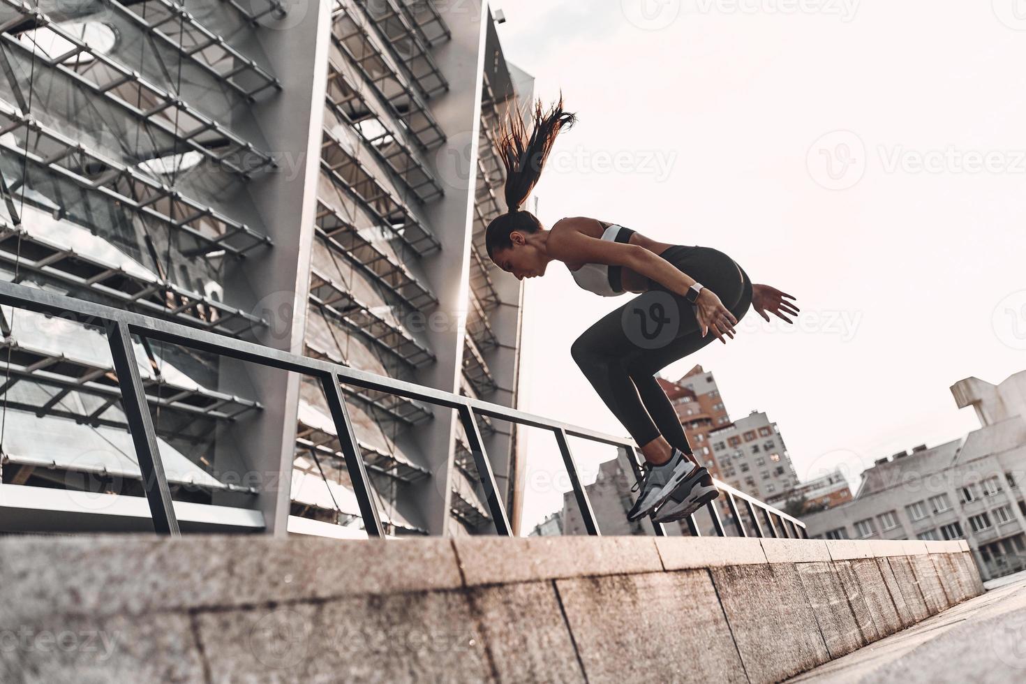 Jumping higher. Full length of modern young woman in sports clothing jumping while exercising outdoors photo