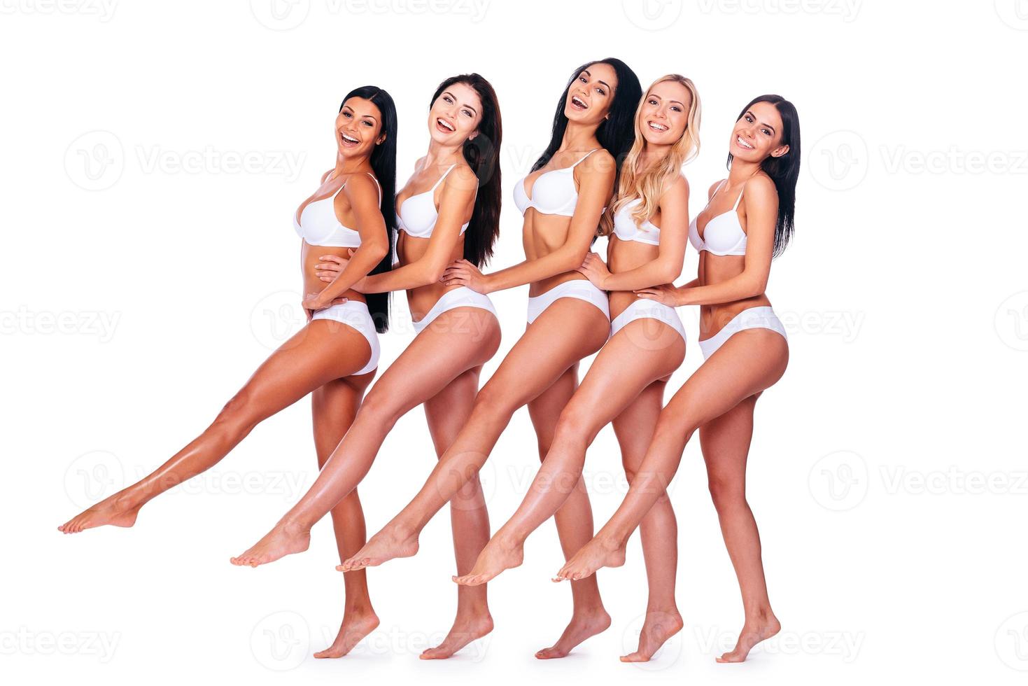 Slender legs. Full length of five beautiful young women in lingerie stretching out their legs and smiling while bonding to each other and standing against white background photo