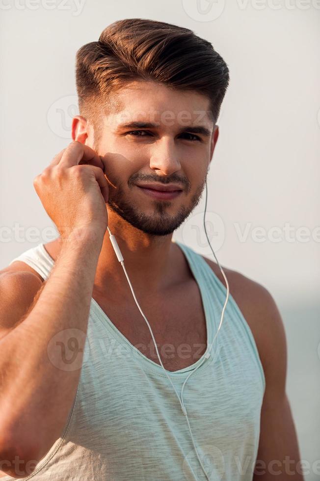 llevar mi música conmigo a la carrera. apuesto joven musculoso en auriculares mirando a la cámara mientras está de pie al aire libre foto