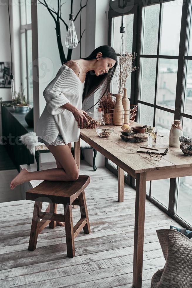 Healthy breakfast. Full length of attractive young woman pouring cereal and smiling while standing near the window at home photo