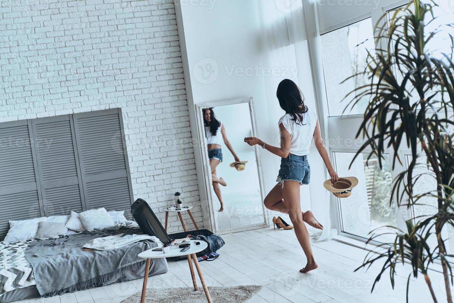 Charming girl at home. Full length rear view of young woman looking in the mirror while standing near the suitcase at home photo