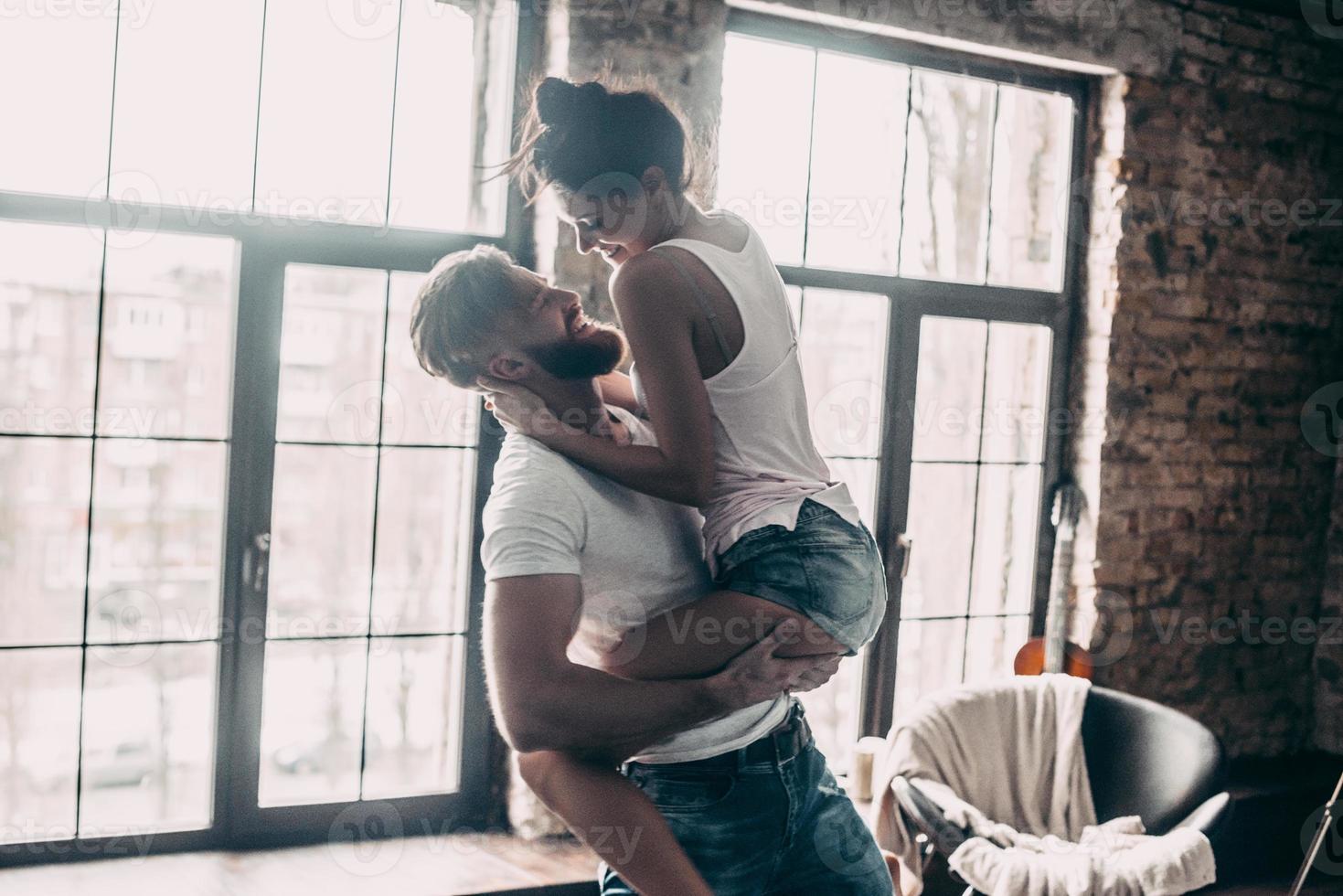 hermosa pareja joven pareja apasionada divirtiéndose juntos y luciendo feliz mientras un joven apuesto lleva a su novia en las manos foto