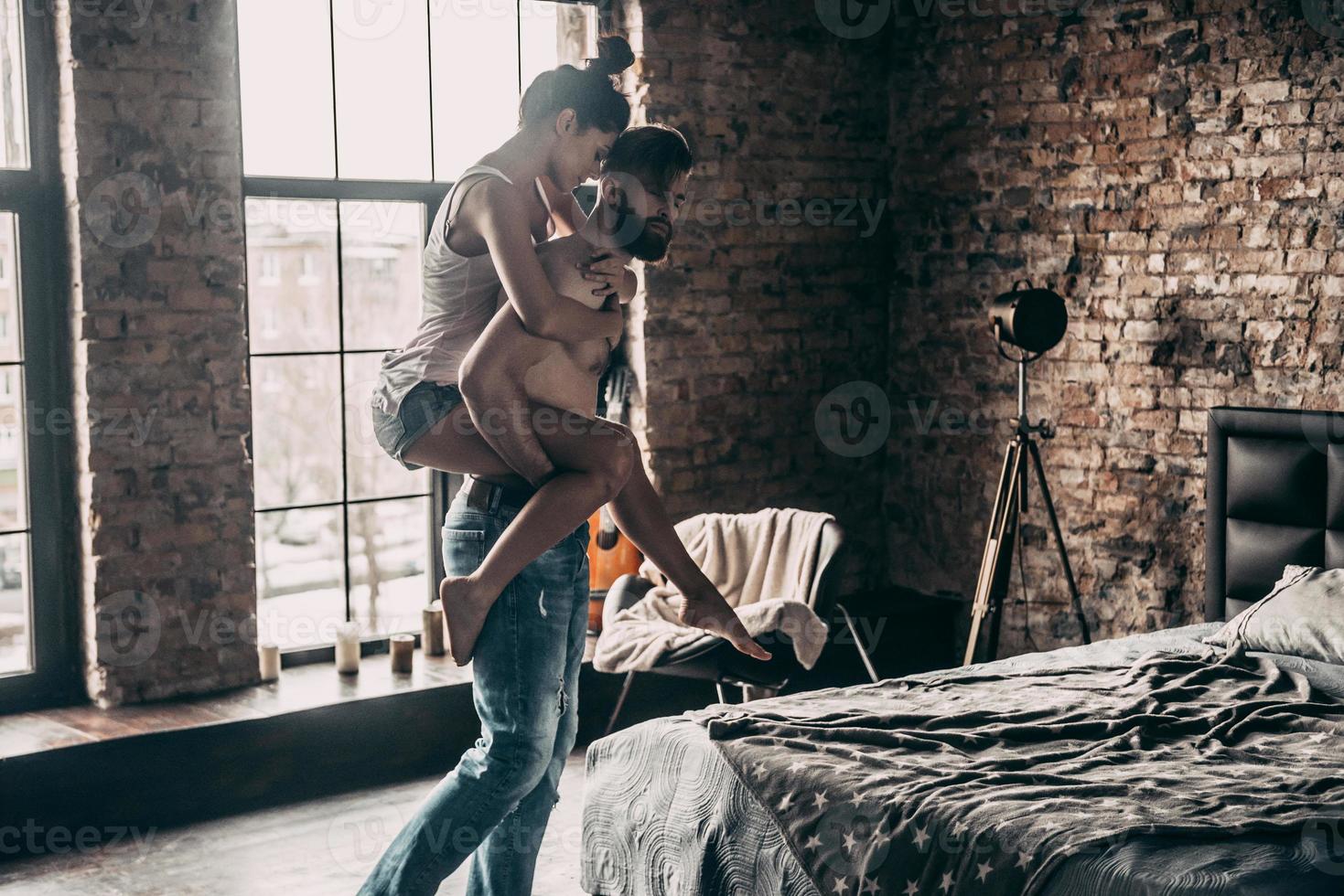 They belong together. Young couple enjoying free time at home while shirtless man carrying attractive woman on shoulders photo