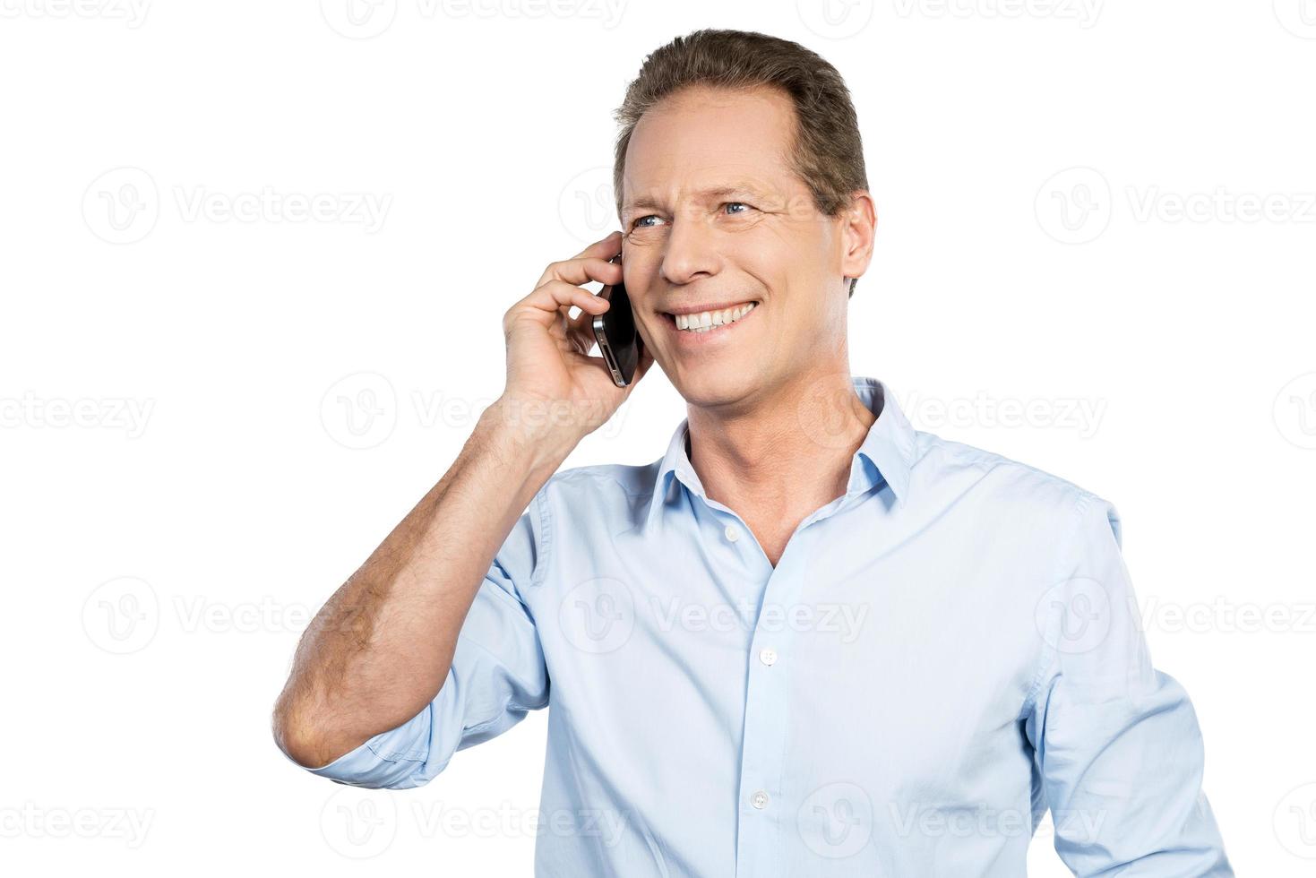 Good talk. Happy mature man talking on the mobile phone and smiling while standing against white background photo