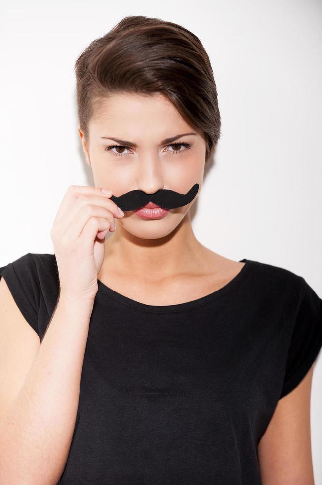 Just for fun. Portrait of beautiful young short hair woman holding fake mustache on her face and looking at camera photo