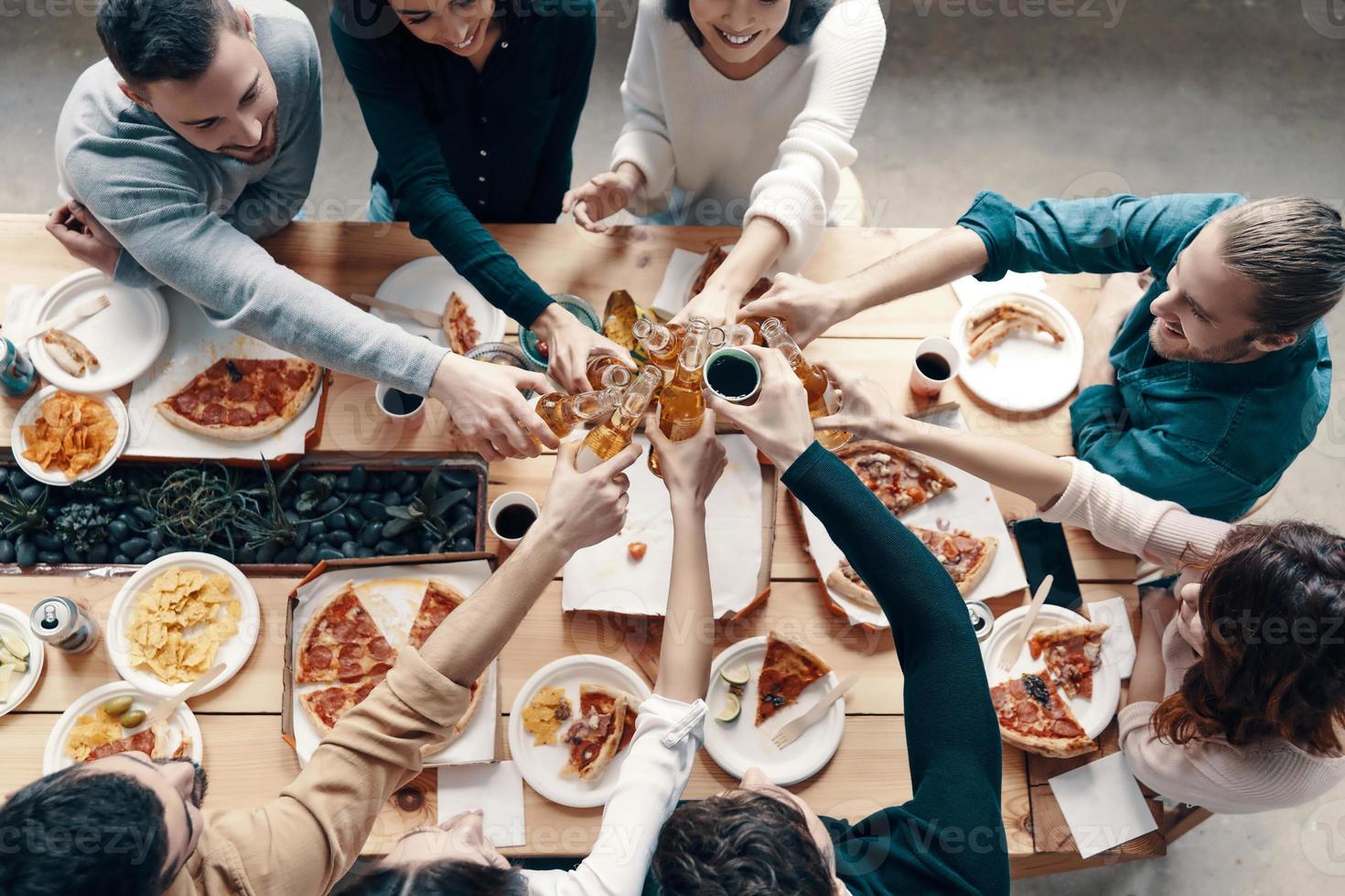 grupo de jóvenes con ropa informal recogiendo pizza y sonriendo mientras cenan en el interior foto