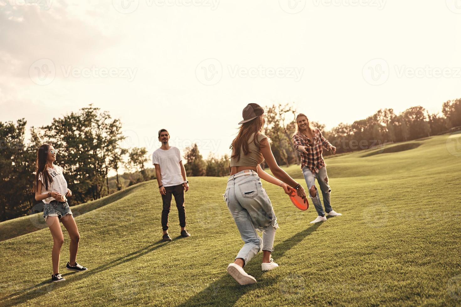 Enjoying game with friends. Full length of young smiling people in casual wear playing Frisbee while spending carefree time outdoors photo