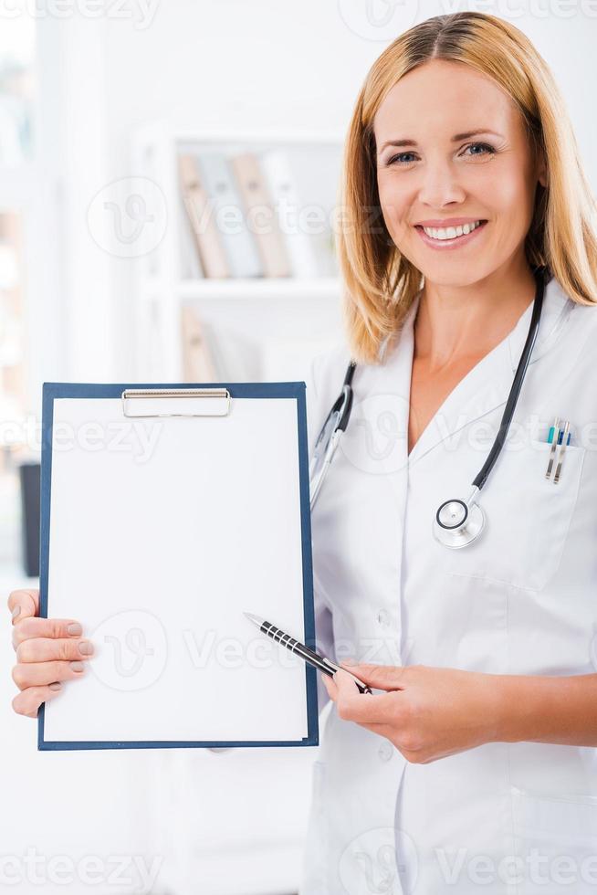 los resultados de su prueba aquí. doctora feliz con uniforme blanco mirando la cámara y sonriendo mientras señala el portapapeles foto