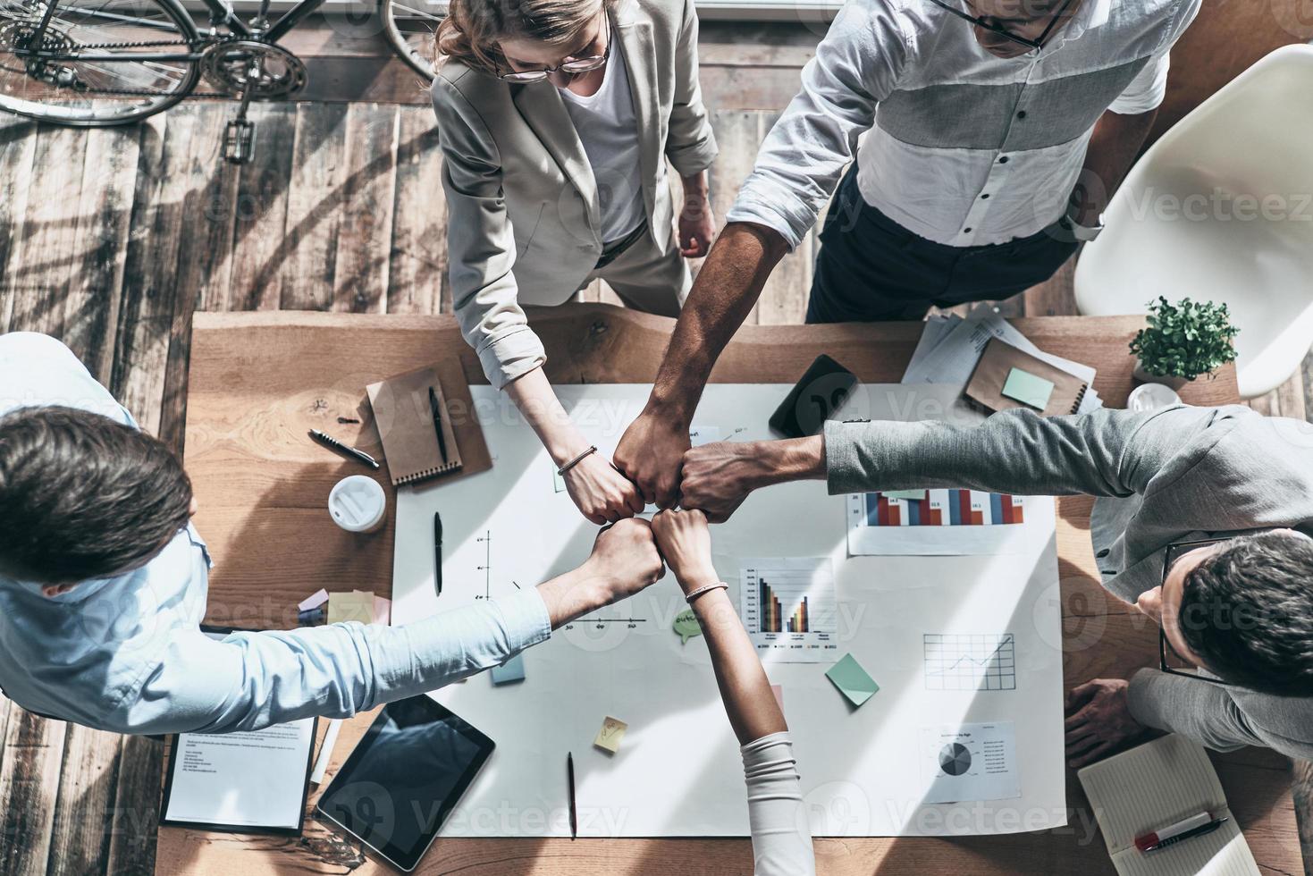 Cooperation. Close up top view of business colleagues holding fists together in a symbol of unity while working in the creative office photo