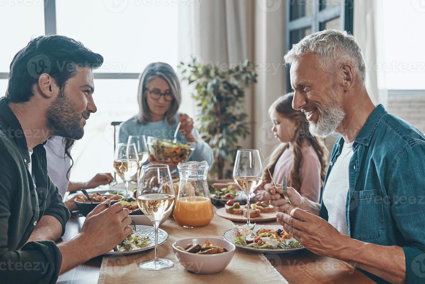 feliz familia multigeneracional comunicándose y sonriendo mientras cenamos juntos foto