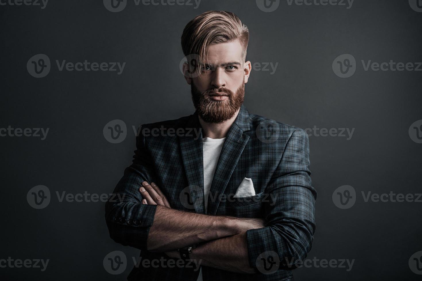 Attractive man with long hair and beard looking at camera while standing against grey background photo