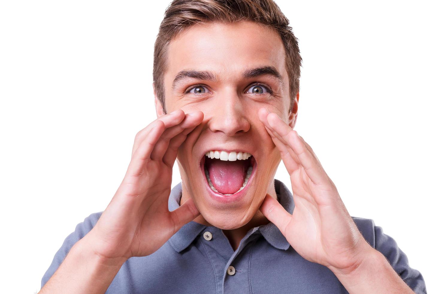 Announcing good news. Happy young man holding hands near mouth and shouting while standing isolated on white background photo