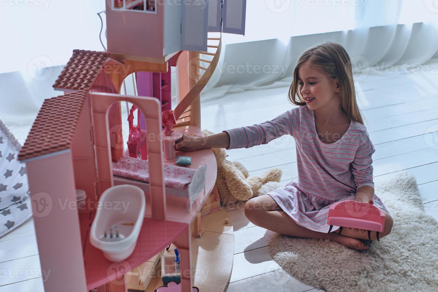 Using fantasy to play. Cute little girl playing with a dollhouse while sitting on the floor in bedroom photo