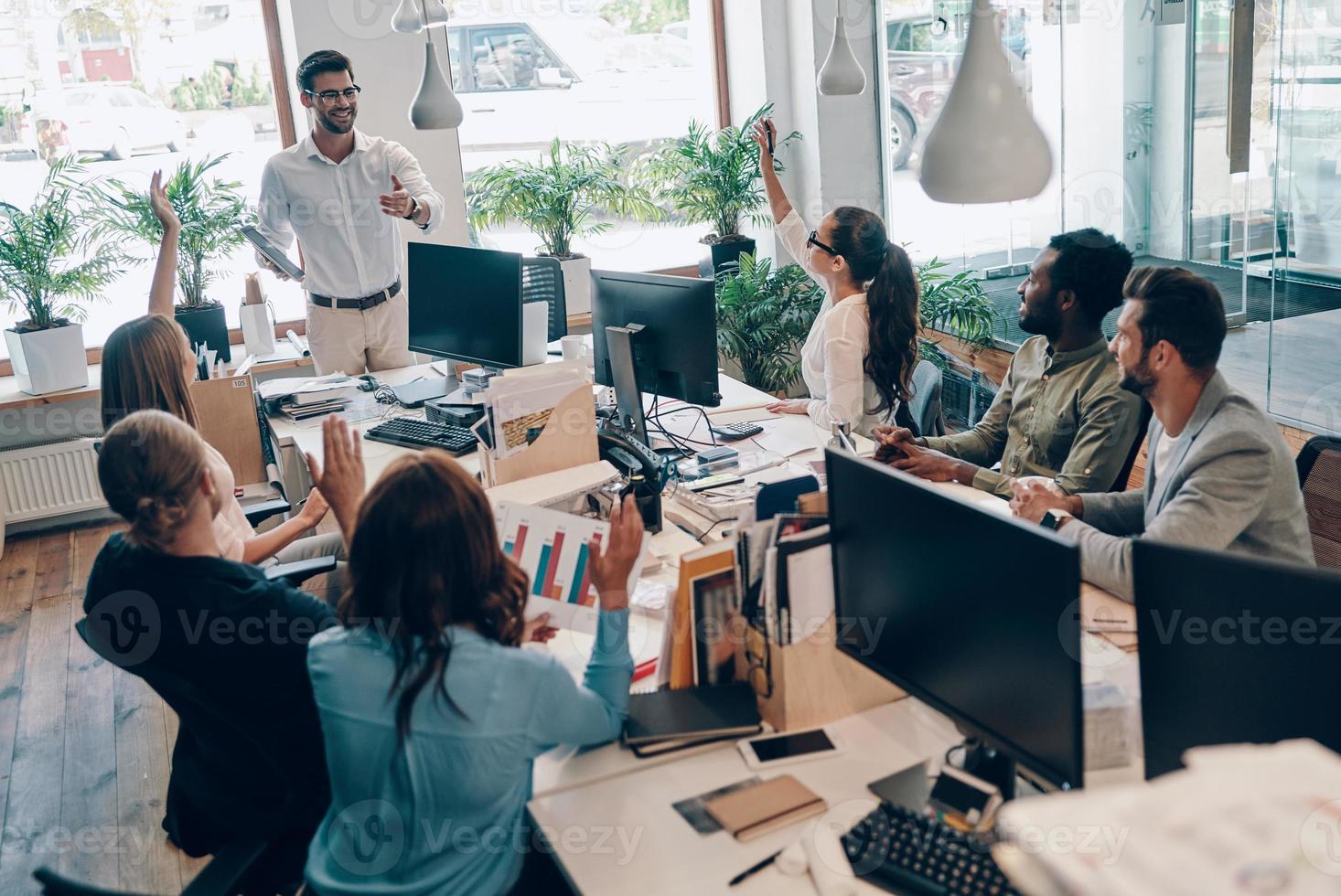 Group of young modern people in smart casual wear communicating and using modern technologies while working in the office photo