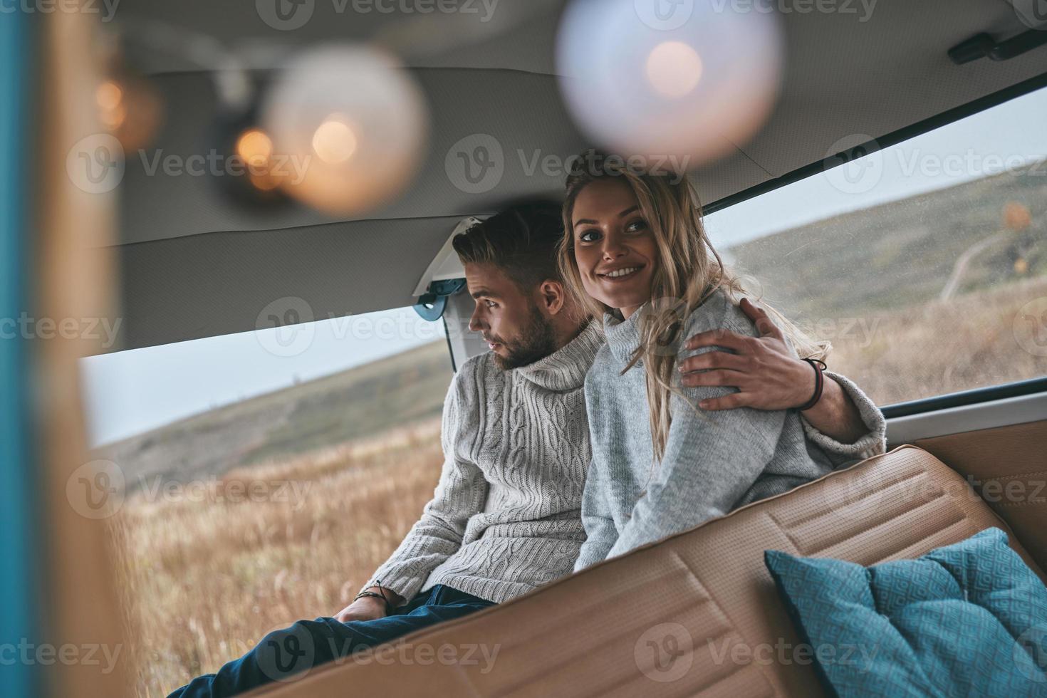 She is the center of his universe. Beautiful young couple resting and smiling while sitting in retro style mini van photo