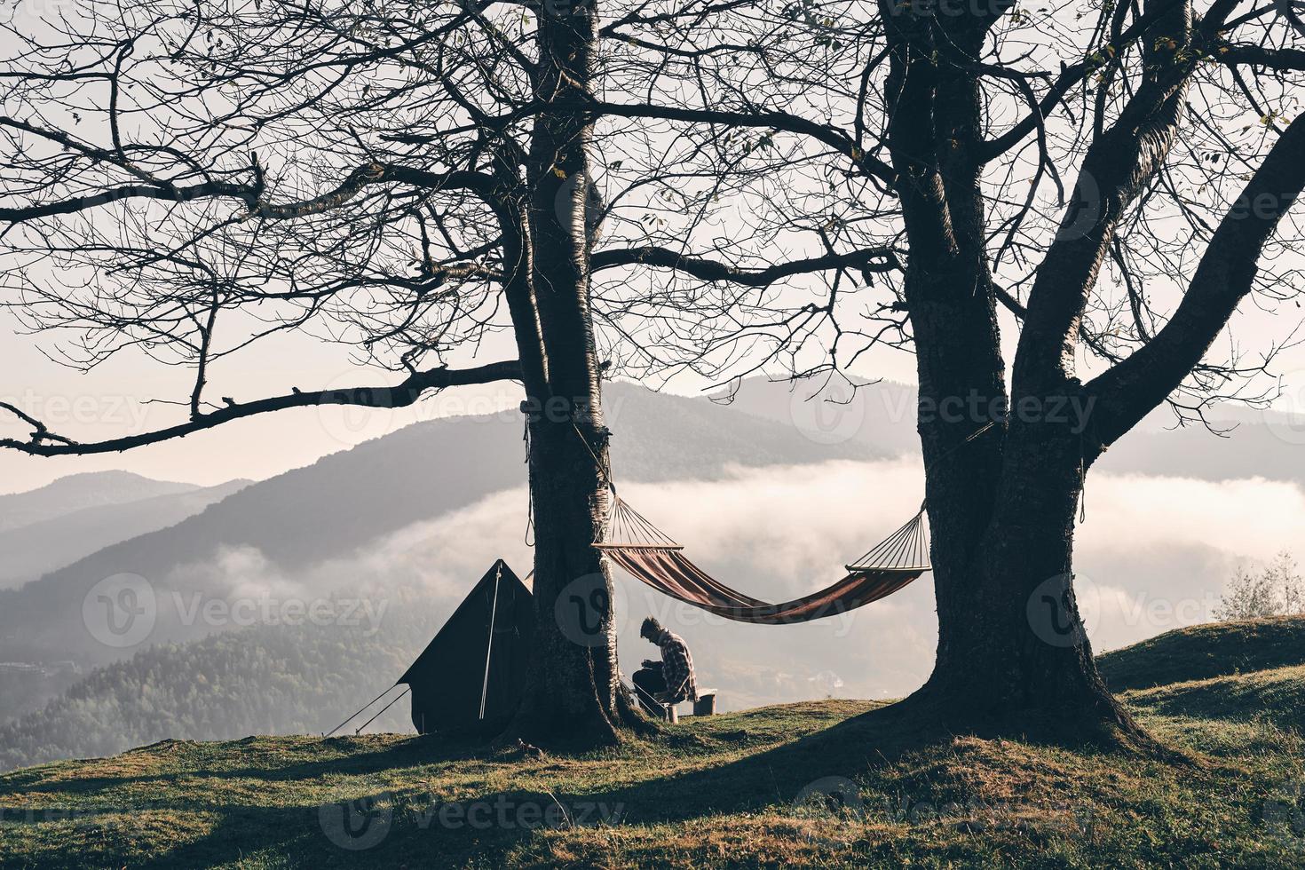 Young man sitting near the tent while camping in the mountains photo