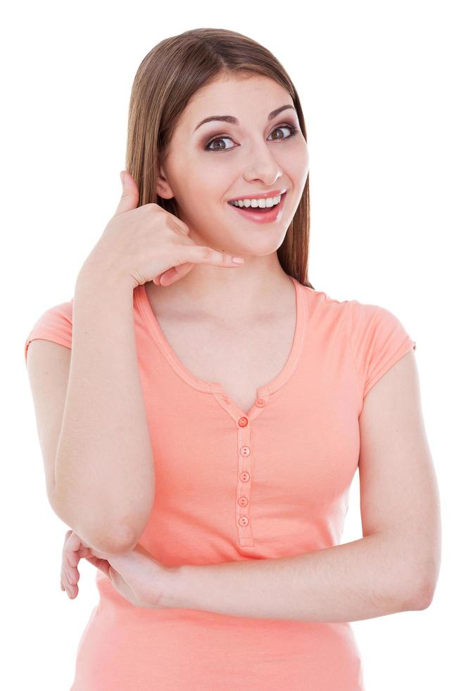 Waiting for your call. Beautiful young smiling woman looking at camera and gesturing mobile phone while standing isolated on white photo