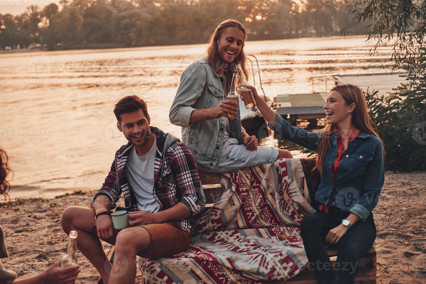 Group of young people in casual wear smiling and taking selfie while enjoying beach party near the lake photo