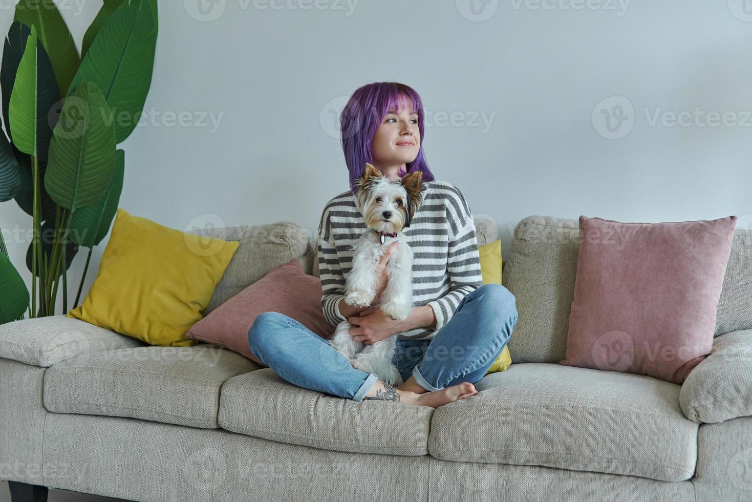 una adolescente alegre que lleva un perrito mientras se relaja en el sofá de casa foto
