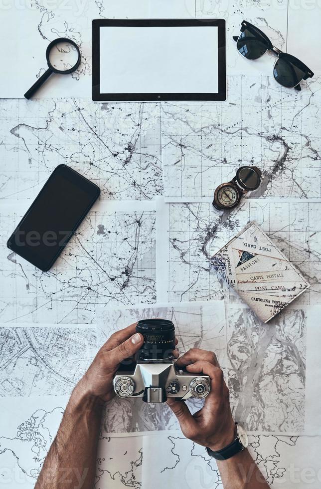 Checking camera. Close up top view of man using photo camera with sunglasses, compass, magnifying glass, smart phone and passport lying on map around