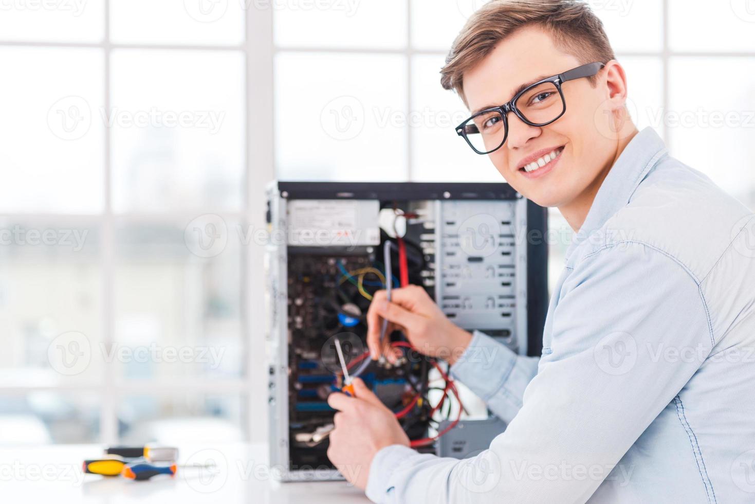 He loves his job. Portrait of handsome young man repairing computer while sitting at his working place photo