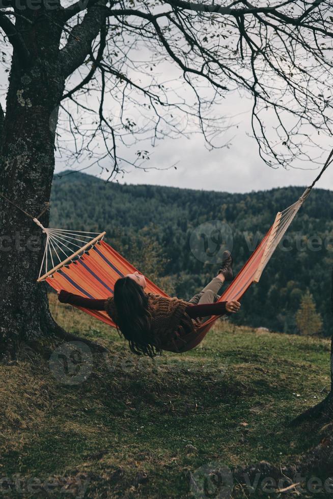 siente la libertad. bella joven tumbada en una hamaca mientras se relaja en el valle bajo el árbol foto