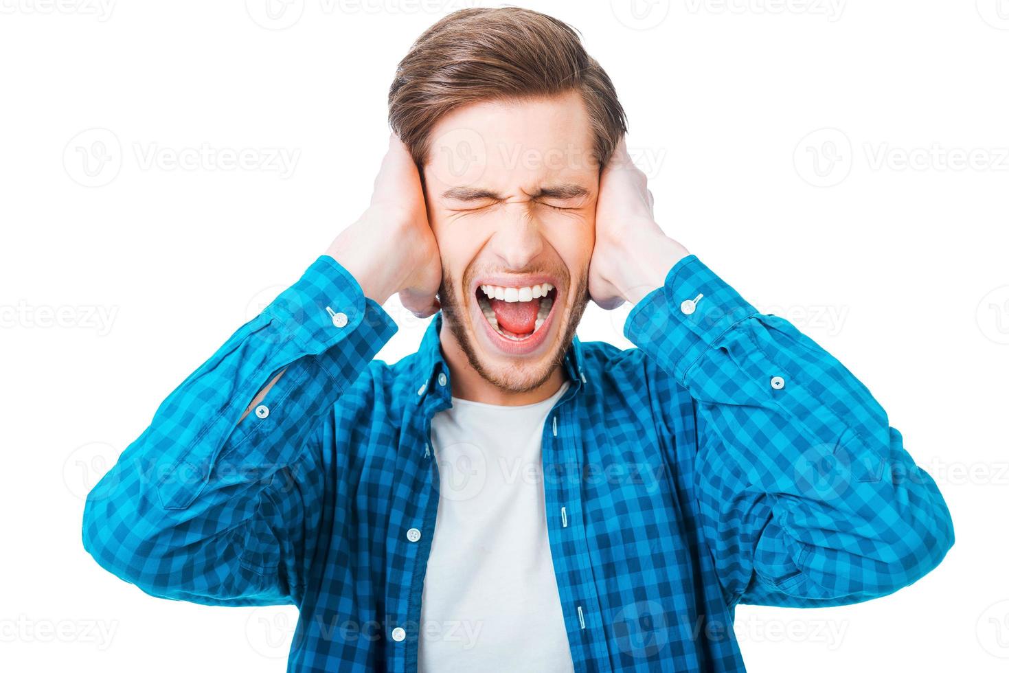 This is too loud Frustrated young man holding head in hands and keeping eyes closed while standing against white background photo