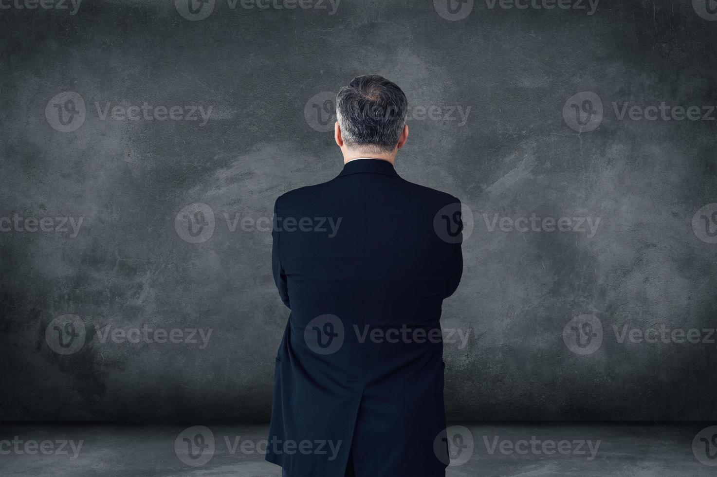 All about confidence. Rear view of mature businessman keeping arms crossed while standing against grey background with copy space photo