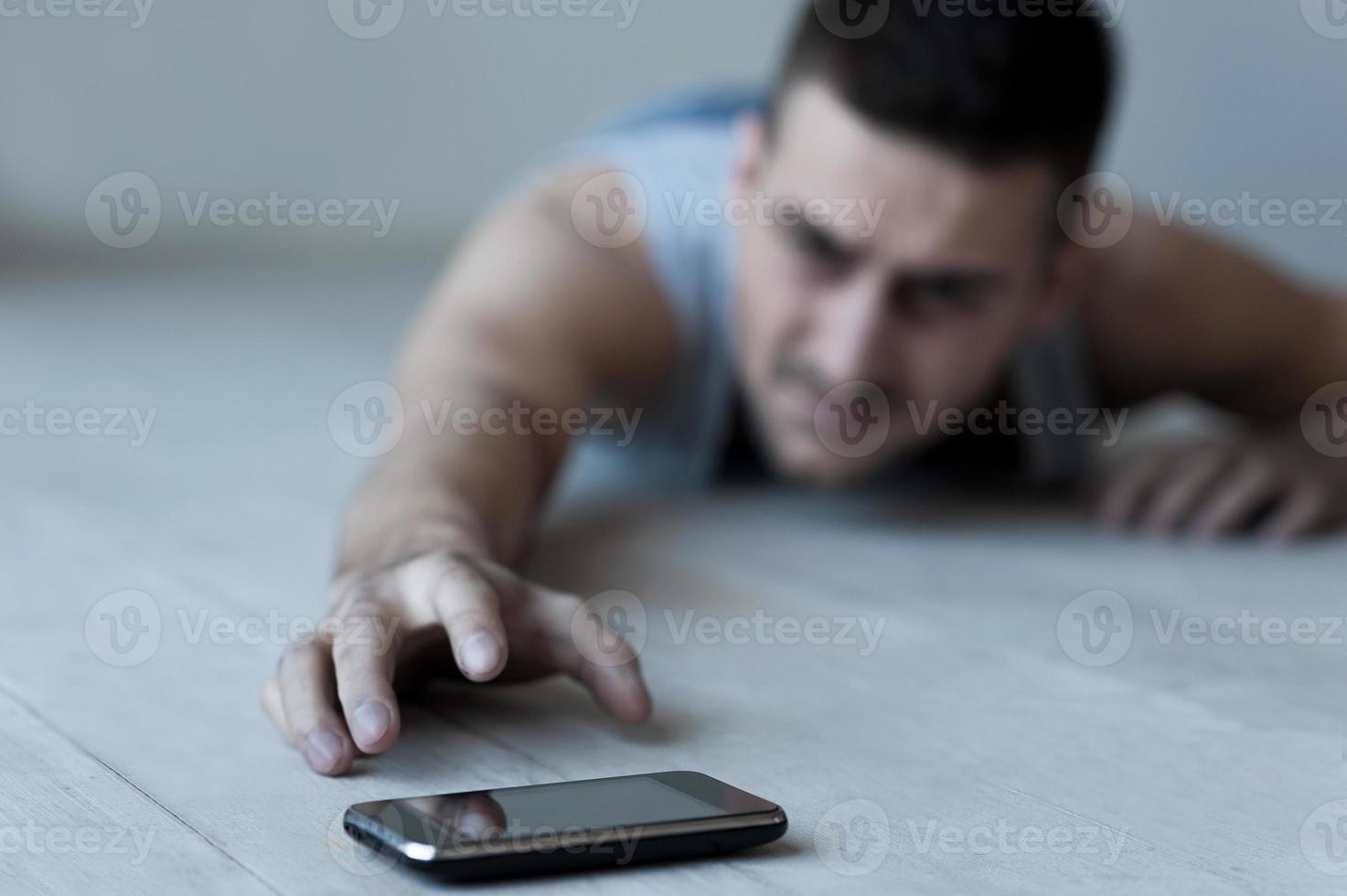 Help me Frustrated young man lying on the floor and stretching hand to the mobile phone photo