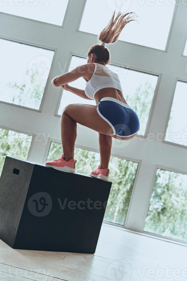 haciendo ejercicio por la mañana. mujer joven moderna en ropa deportiva saltando y agachándose mientras hace ejercicio en el gimnasio foto