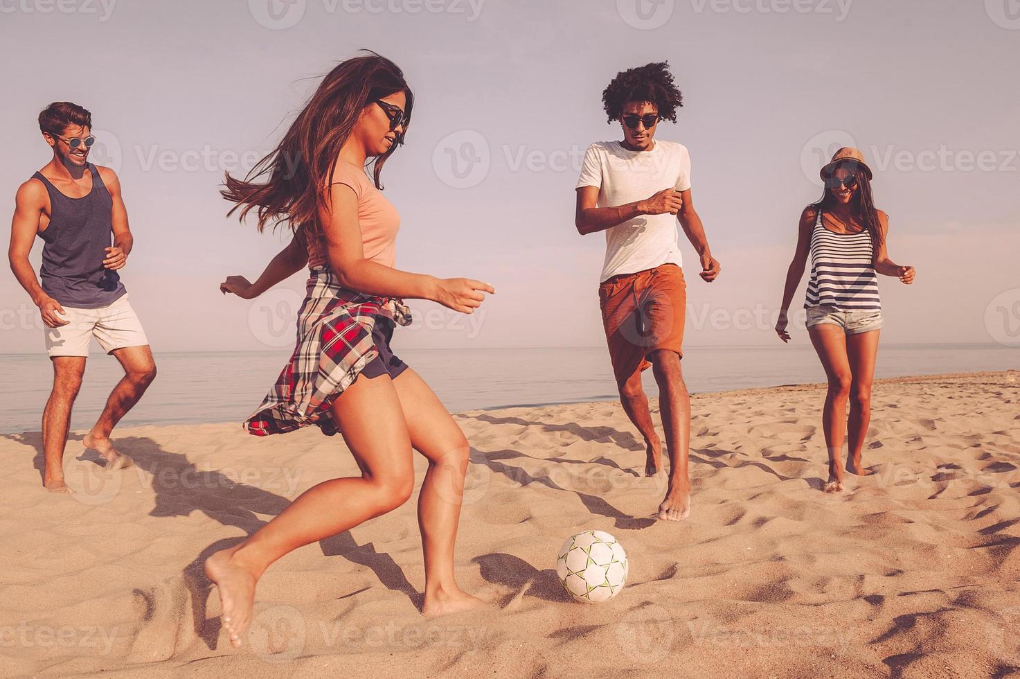 disfrutando del tiempo con los mejores amigos. grupo de jóvenes alegres jugando con una pelota de fútbol en la playa con el mar de fondo foto