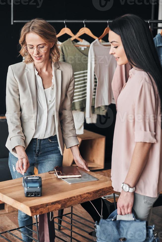 pagos rápidos. vendedor que usa terminal de pago para confirmar la compra y sonríe mientras trabaja en la boutique de moda foto