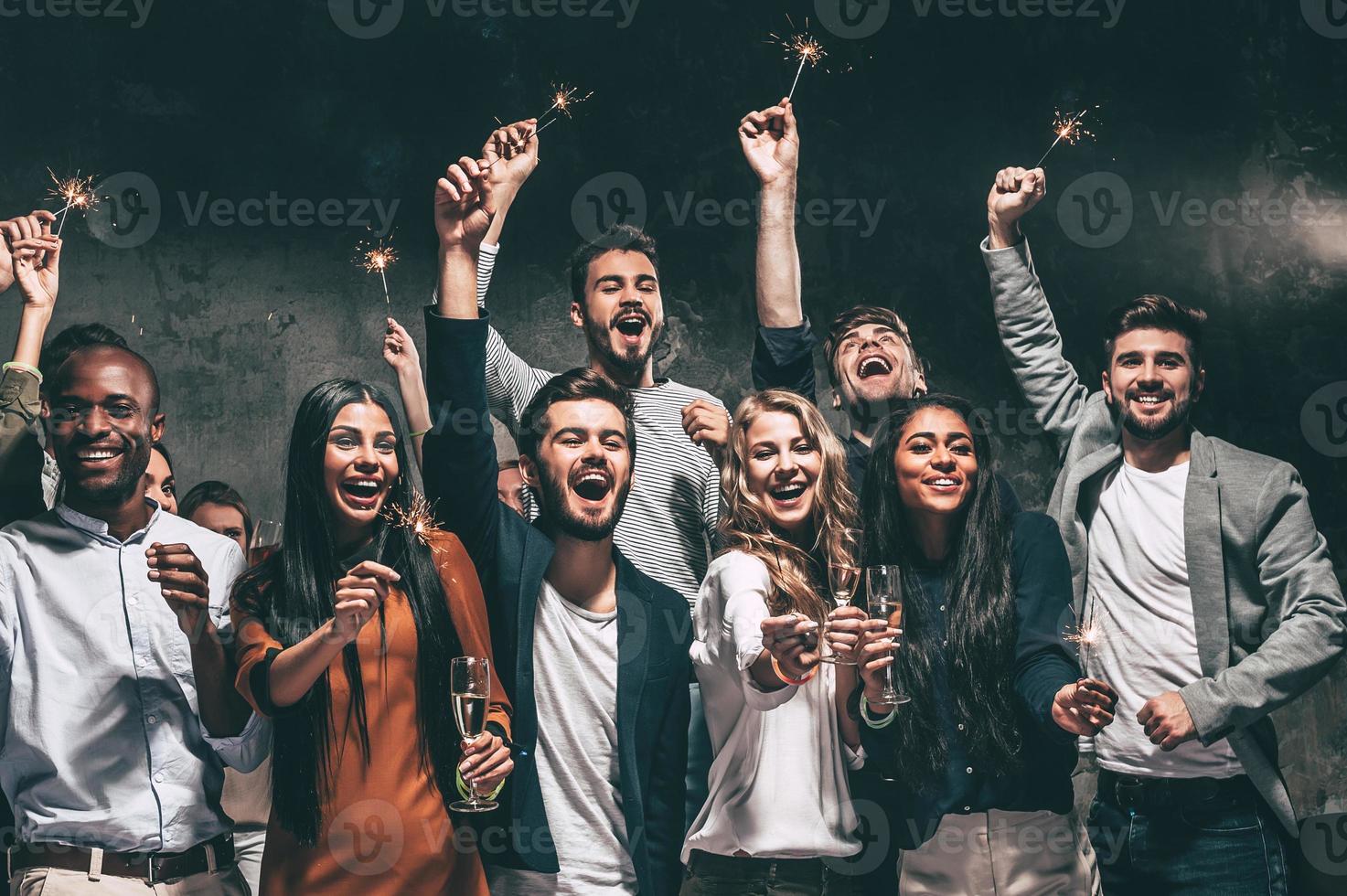 Celebrating with fun. Group of cheerful young people carrying sparklers and champagne flutes photo