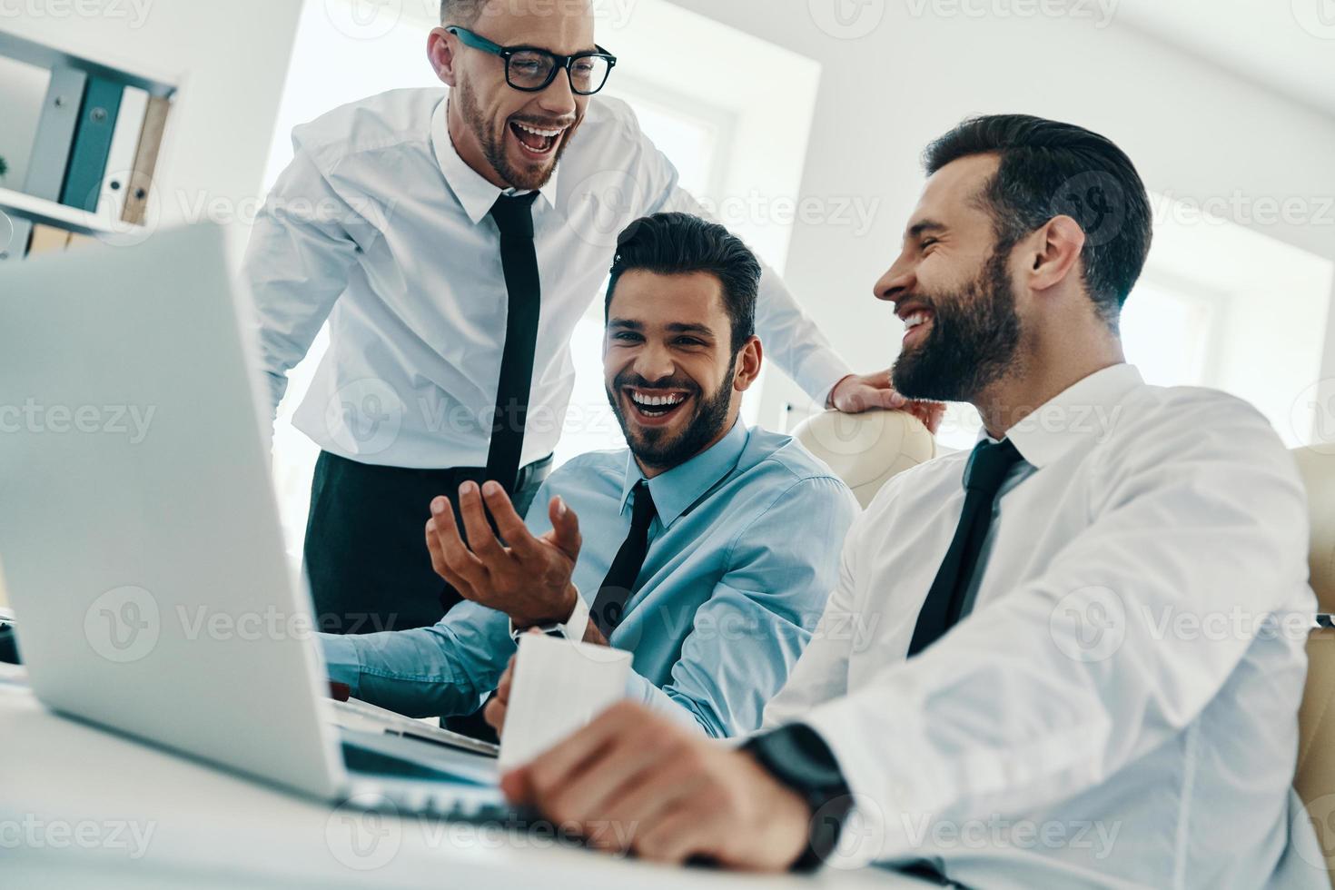 Happy to work together. Group of young modern men in formalwear working using computers and smiling while sitting in the office photo