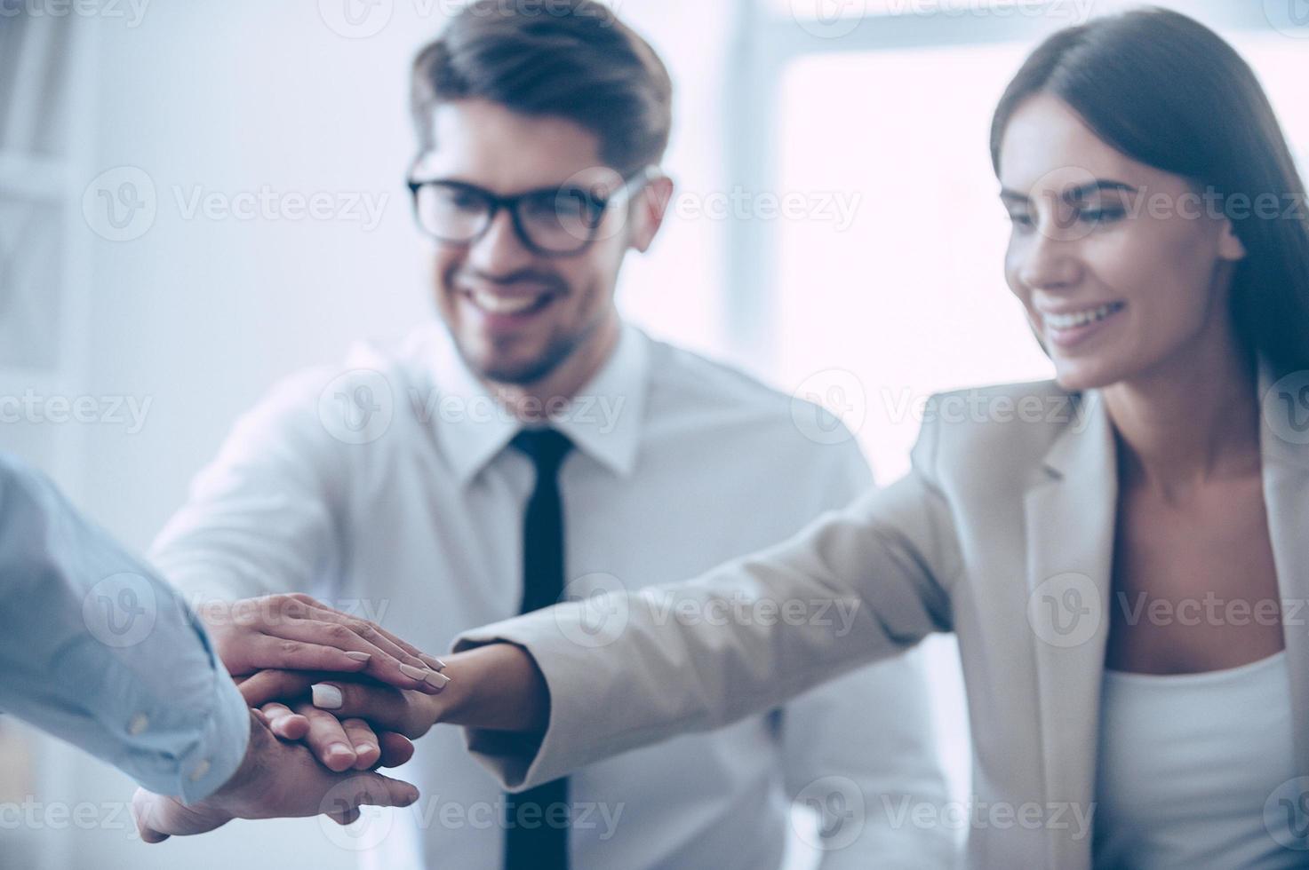 Let us go Close-up part of top view of group of four young people holding hands and showing their unity with smile while sitting at office photo