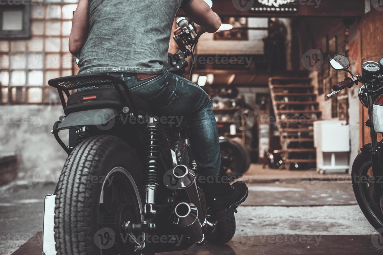On the way to garage. Close-up rear view of man sitting on his bike with motorcycle garage in the background photo