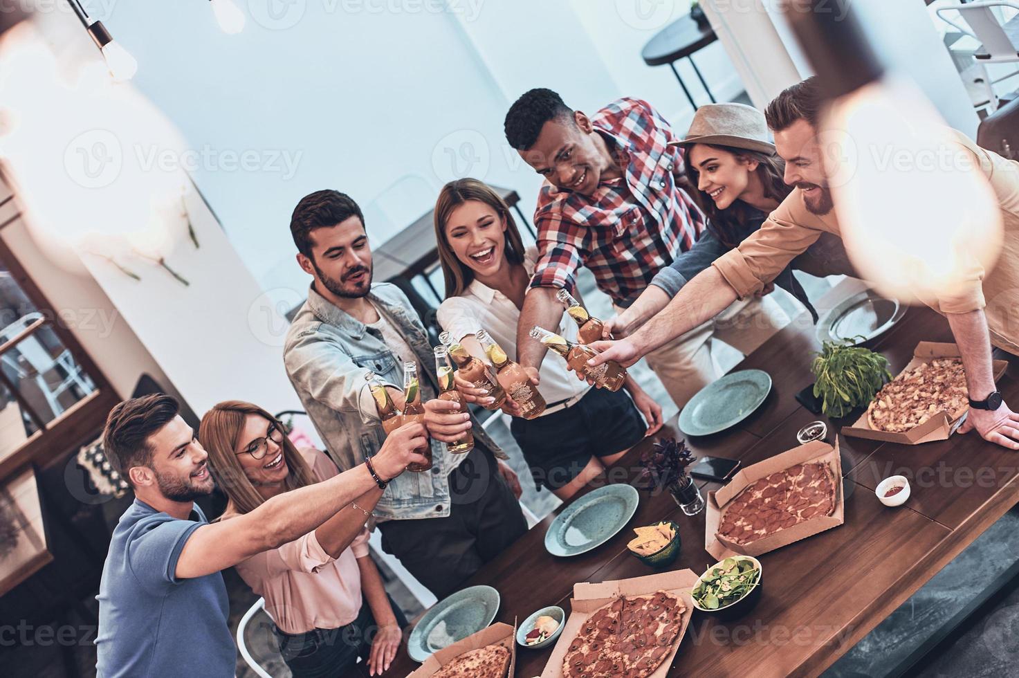 Top view of young people in casual wear gesturing and smiling while having a dinner party indoors photo