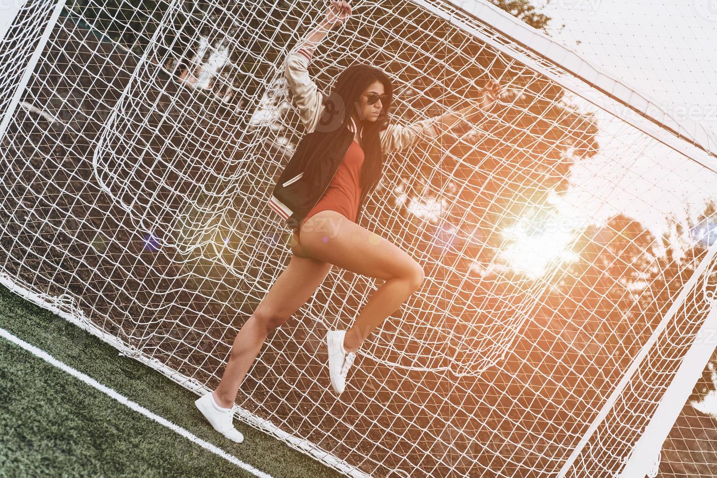 Best goalkeeper ever. Full length of attractive young woman in red bikini leaning at the net while standing at the goal post outdoors photo