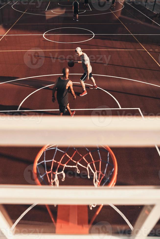 Two young men in sports clothing playing basketball and smiling while spending time outdoors photo