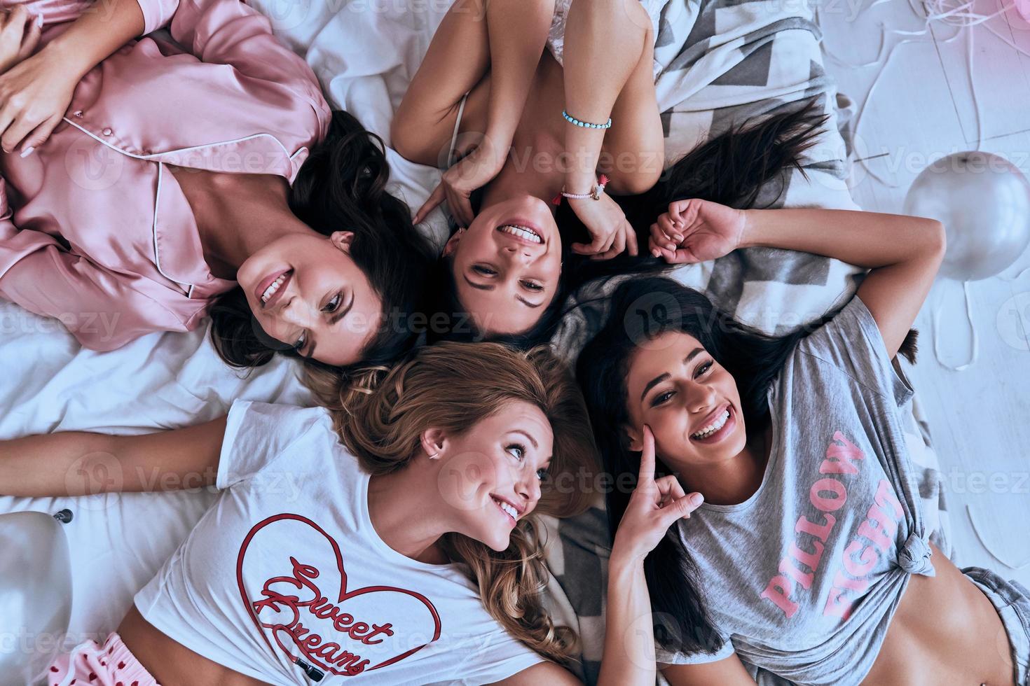 Real fun. Top view of four playful young women smiling while lying on the bed at home photo