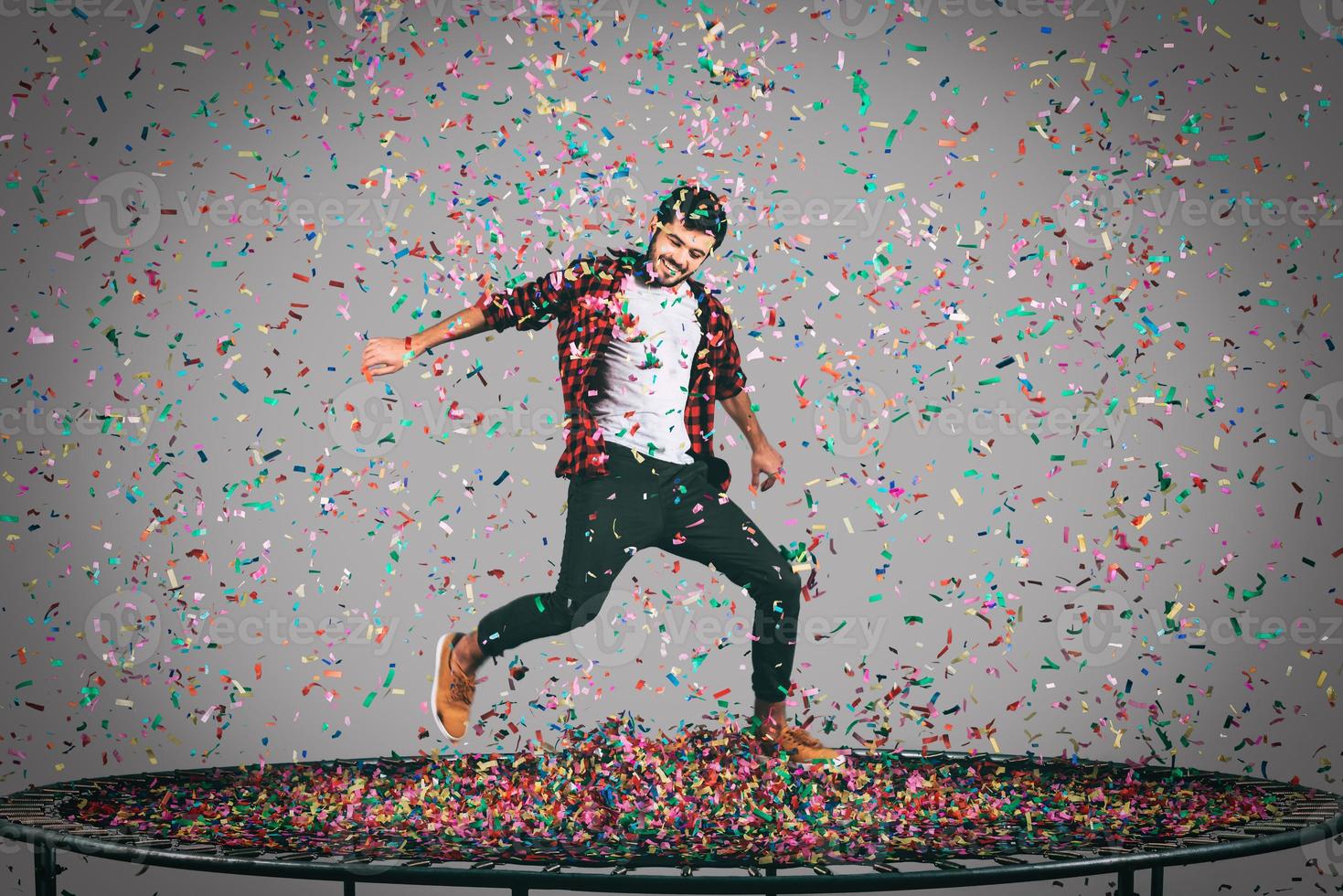 Trampoline and confetti. Mid-air shot of handsome young man jumping on trampoline with confetti all around him photo