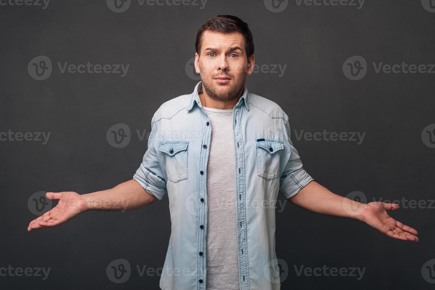 What else can I do Young man keeping arms outstretched and looking at camera while standing against grey background photo