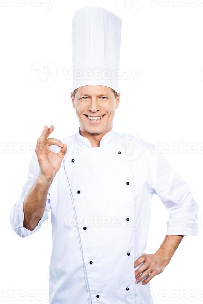 Confident chef. Confident mature chef in white uniform gesturing OK sign and smiling while standing against white background photo