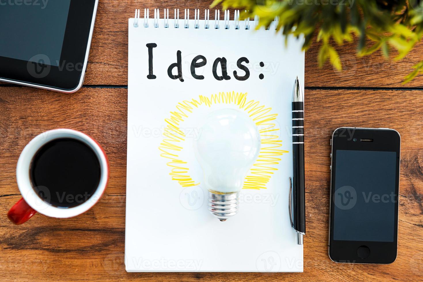 Coffee for fresh ideas. Top view of note pad with coffee cup laying on the wooden desk with different business stuff around it photo