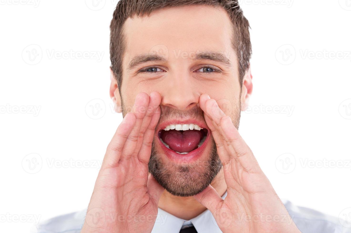 Great news Cheerful young man in formalwear holding hand near mouth and shouting while standing isolated on white background photo