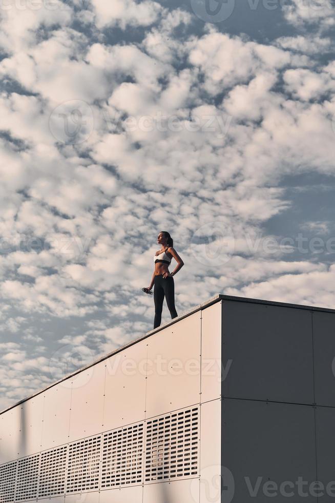 After great workout. Modern young woman in sports clothing relaxing while standing on the roof outdoors photo