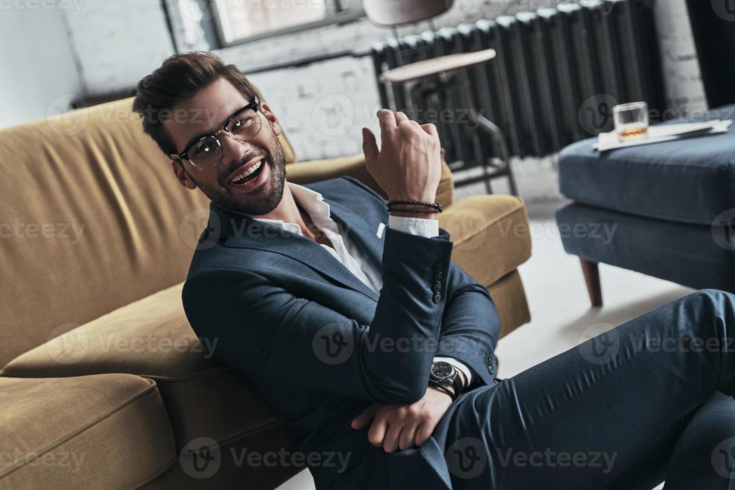 Ready to break hearts. Handsome young man in full suit smiling and looking away while sitting on the floor at home photo